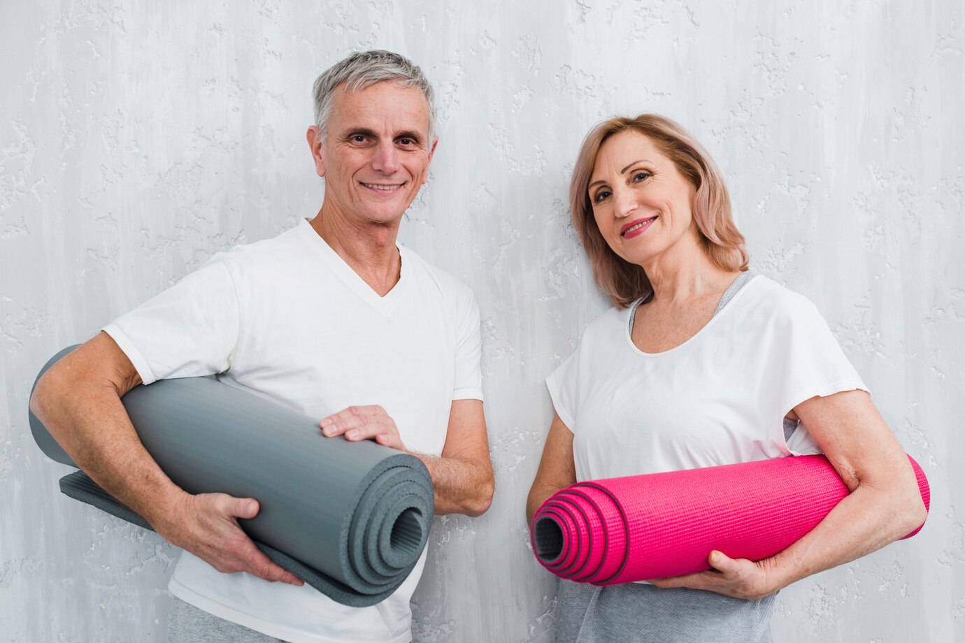 happy-couple-holding-leaning-white-wall-holding-rolled-yoga-mat_23-2148097482